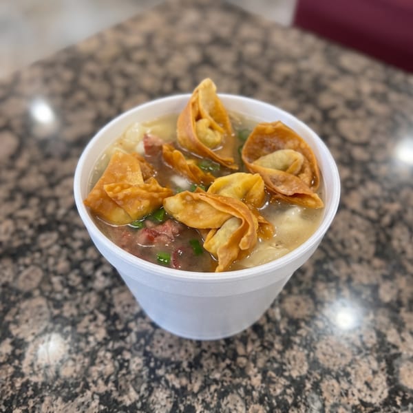 Wonton soup with fried dumplings, beef, and scallions in a white bowl on a granite table.