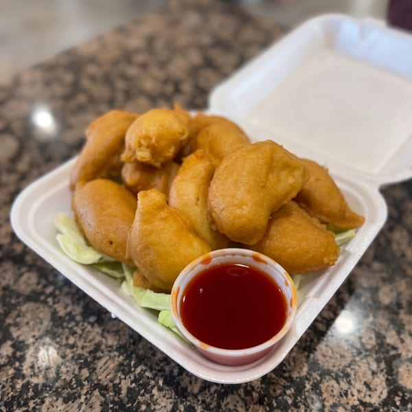 Golden-brown fried nuggets with red dipping sauce and lettuce in a white takeout container.