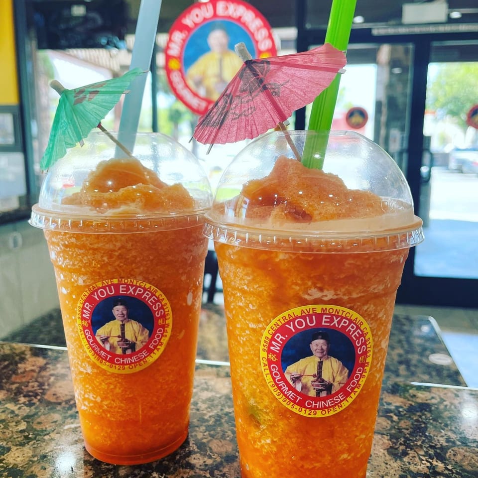 Two orange frozen drinks with straws and umbrellas on a counter at Mr. You Express.