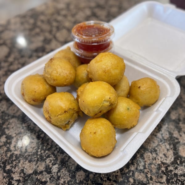 Golden-brown fried balls in a white takeout container with two cups of red dipping sauce.