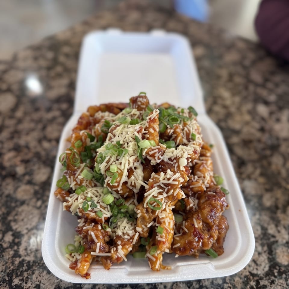 Saucy fries topped with shredded cheese and green onions in a white takeout container.
