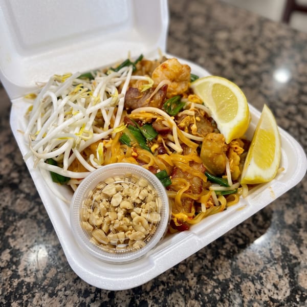 Shrimp Pad Thai with bean sprouts, green onions, lemon, and peanuts in a takeout container.
